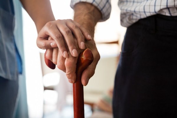 assistant's hand on elderly person's hand holding cane